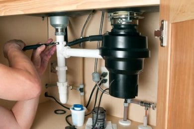 Plumber repairing a garbage disposal beneath a kitchen sink in Silver Spring