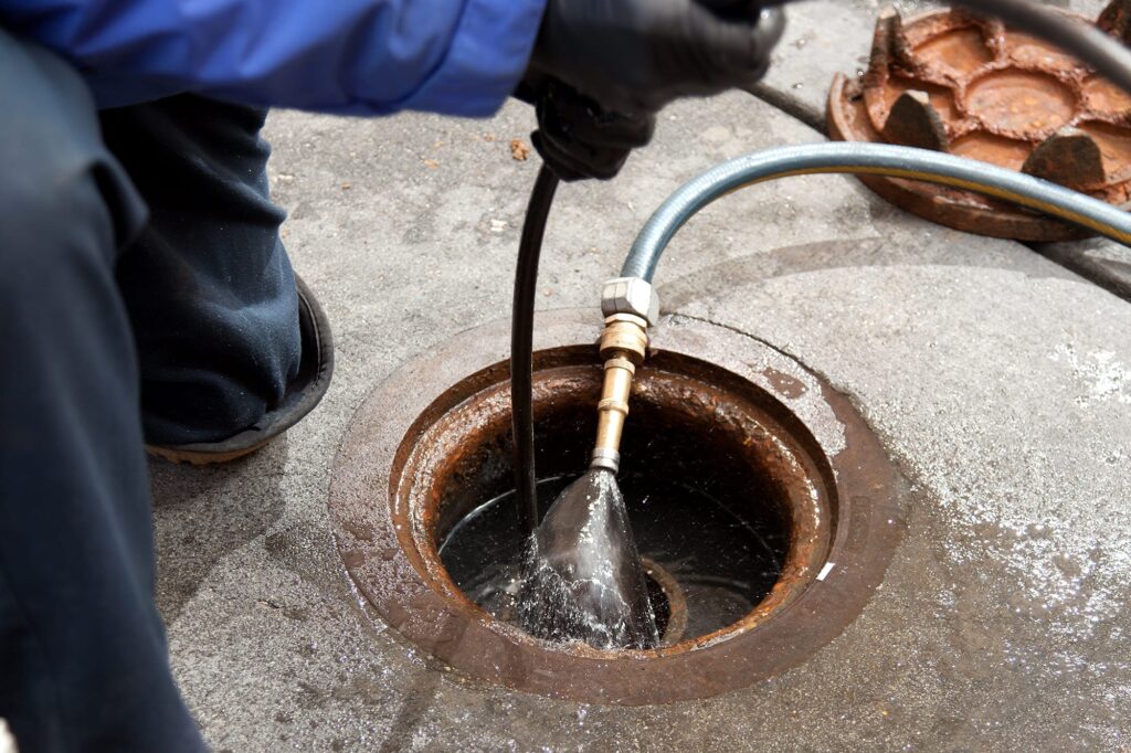 Plumber hydro jetting a sewer line through a manhole in Silver Spring