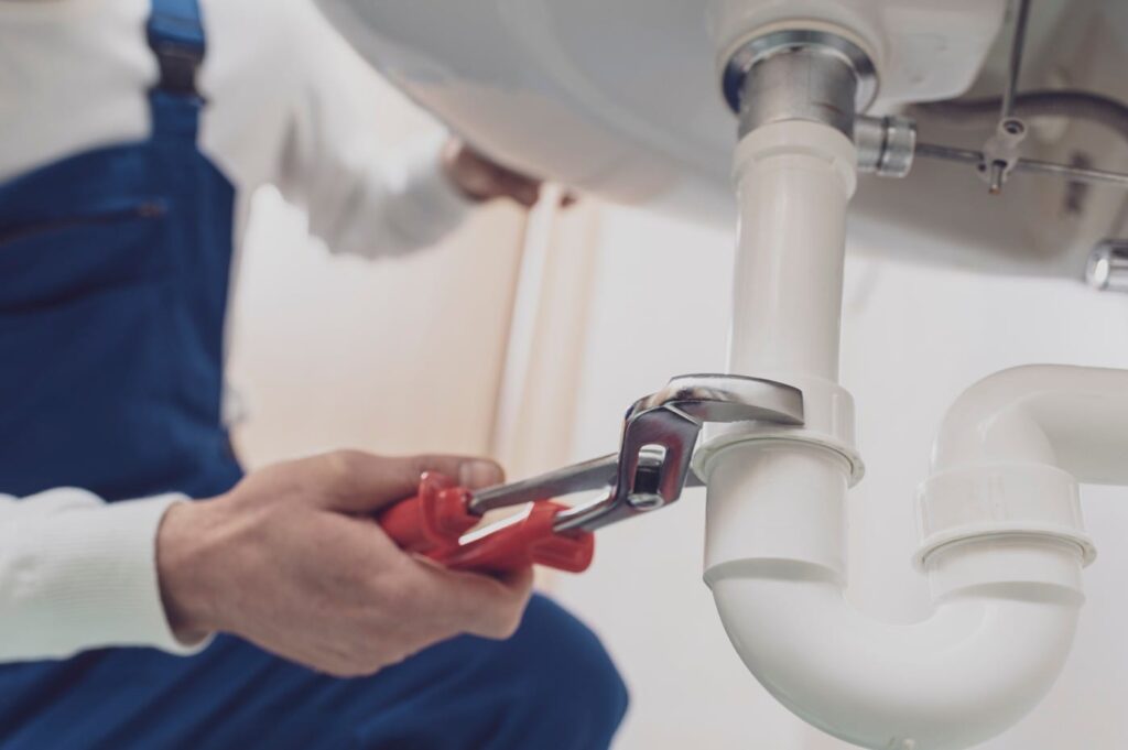 Plumber repairing a white drain pipe beneath a sink in Silver Spring